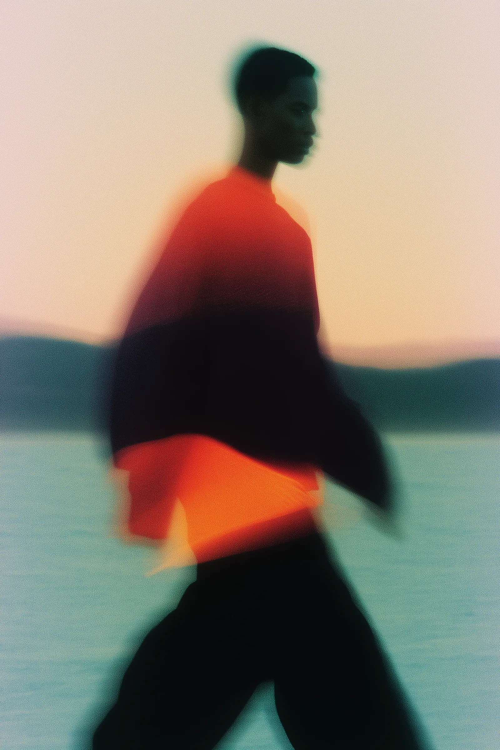 Blurred silhouette of a person in red and black walking outdoors at sunset, with a dreamy pastel toned background